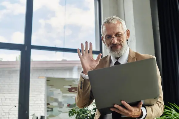 Uomo di mezza eta 'in giacca e cravatta, con la barba, che insegna online. Sorride, saluta gli studenti, creando uno spazio di apprendimento accogliente — Foto stock