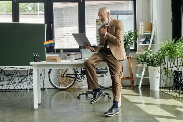 A middle-aged gay teacher, wearing a suit and glasses, stands by a desk in a modern office, teaching online. — Stock Photo