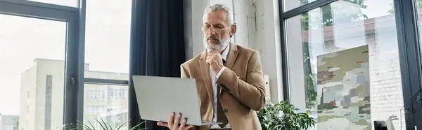 A mature LGBTQ teacher with a beard uses his laptop to teach a class online from a modern office space. — Stock Photo