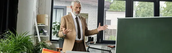 A middle-aged teacher with a beard teaches a class online using a laptop and a whiteboard. — Stock Photo