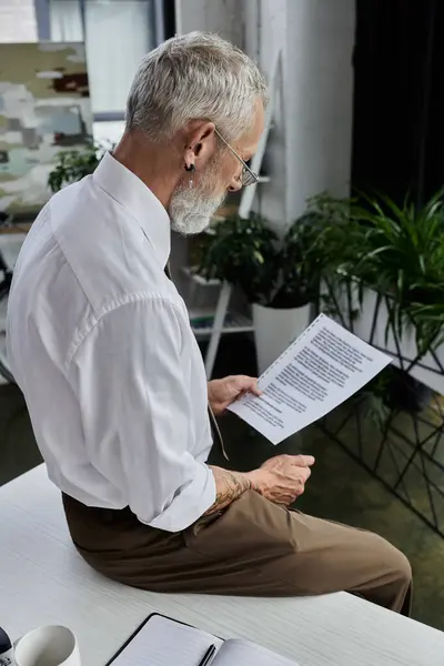 Un insegnante maturo con la barba si siede alla sua scrivania, rivedendo gli appunti per un corso online. — Foto stock
