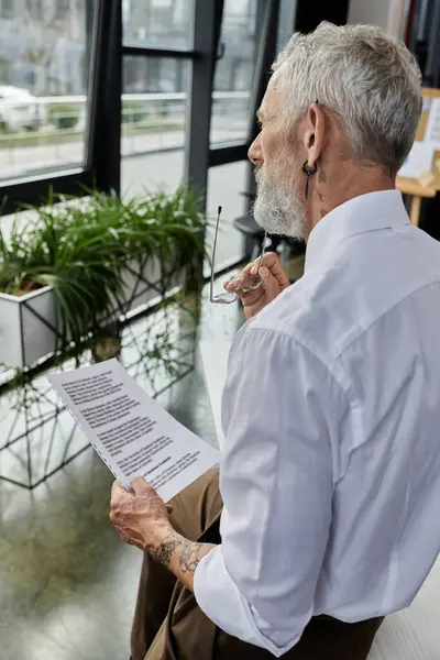 A mature LGBTQ teacher with a beard reads a document while teaching online. — Stock Photo