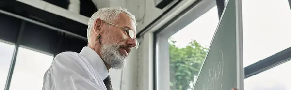 Un homme aux cheveux gris et à la barbe, portant une chemise blanche, enseigne une classe en ligne. — Photo de stock