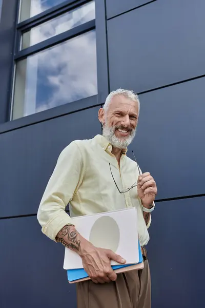 A middle-aged man with a beard smiles at the camera while holding a stack of papers. — Stock Photo