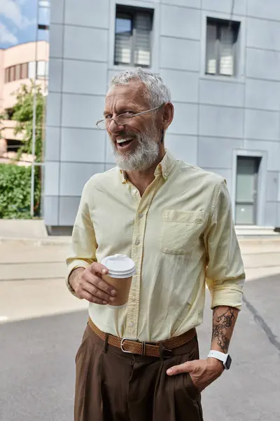 A middle-aged man with a beard smiles and holds a cup of coffee outside a modern building. — Stock Photo