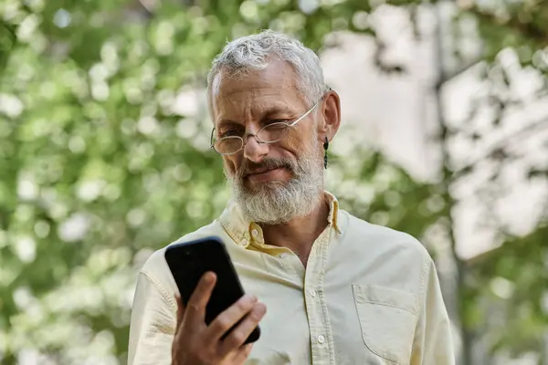 A middle-aged man with a beard checks his phone while standing outside. — Stock Photo