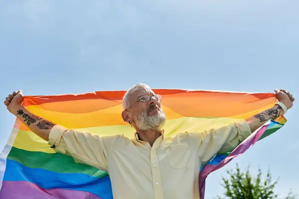 A middle-aged man with a beard holds a rainbow flag high in the air. — Stock Photo