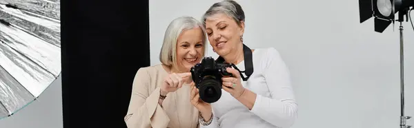 Дві зрілі жінки, фотограф і її модель, переглядають фотографію разом у студії. — стокове фото