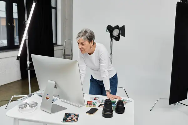 A woman leans over a computer in a photo studio, reviewing images with a serious expression. — Stock Photo