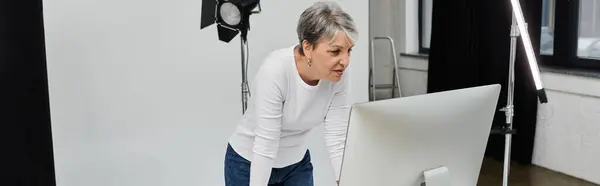 A woman in a white shirt bends over a computer screen, likely reviewing photos of a photoshoot. — Stock Photo