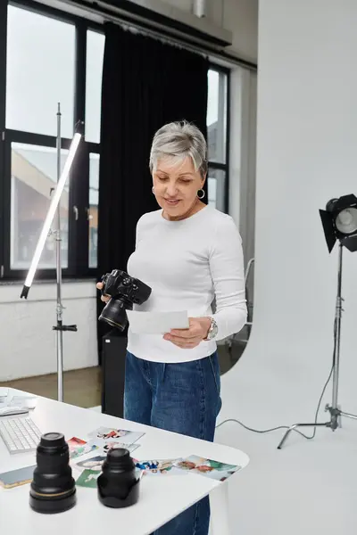 Eine reife Fotografin begutachtet Fotos auf einem Tisch im Fotostudio. — Stockfoto