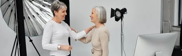 Two mature women, one a photographer and the other a model, share a lighthearted moment during a photo shoot. — Stock Photo