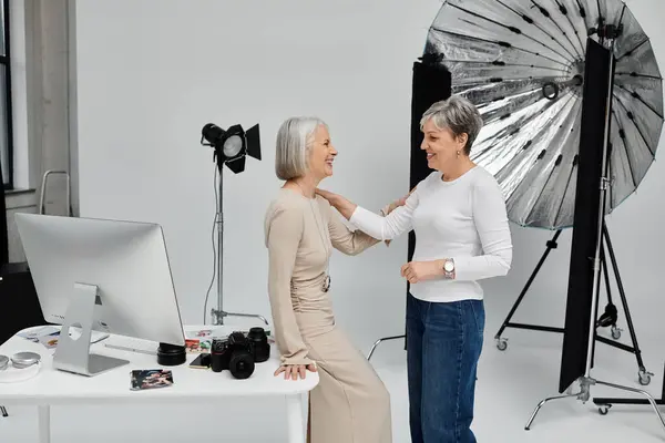 A photographer adjusts the pose of her model in a photography studio, both women smiling and laughing. — Stock Photo
