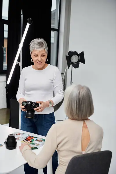 Eine Frau hält eine Kamera in der Hand und schaut die Frau an, die vor ihr sitzt, beide lächeln in einem Studio-Setting. — Stockfoto