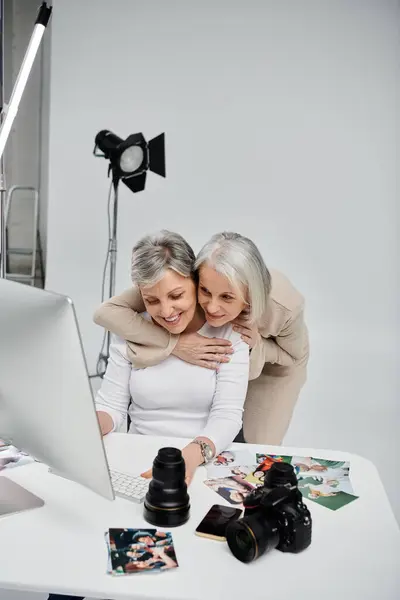 A lesbian couple poses for photos in a studio, one woman hugging the other from behind as they look at the computer screen. — Stock Photo