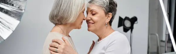 Due donne lesbiche mature abbracciano, una fotografa, l'altra modella, in uno studio fotografico. — Foto stock