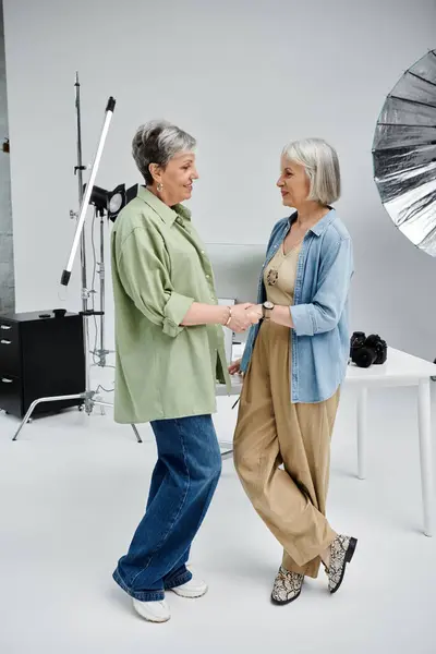Дві зрілі лесбіянки в фотостудії, одна позує як модель, інша фотографує. — стокове фото