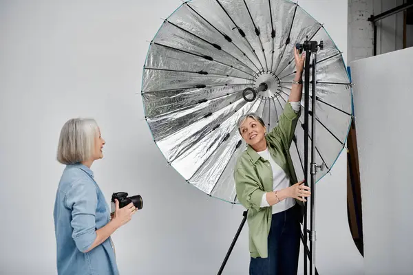 A lesbian couple enjoys a fun photoshoot in a studio, with one woman adjusting a reflector and the other holding a camera. — Stock Photo