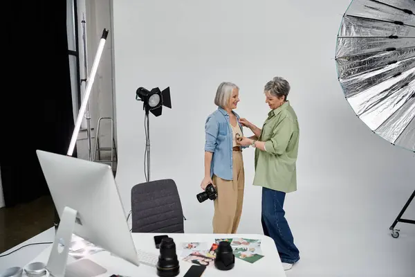 Deux femmes posent dans un studio de photographie, l'une ajustant l'autre vêtements lorsque l'appareil photo clique. — Photo de stock