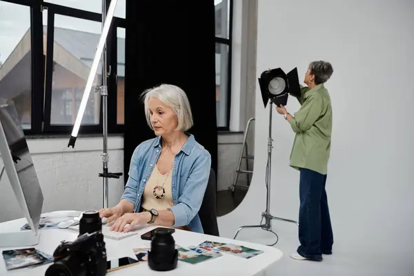 A photographer edits photos on a computer while her partner adjusts the lighting in a photo studio. — Stock Photo