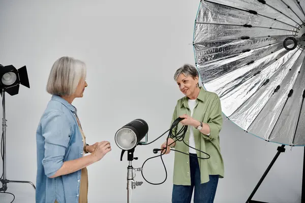A mature lesbian couple works together in a photo studio, one as the photographer, the other as the model. — Stock Photo