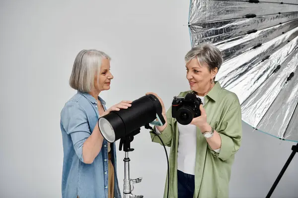 Две зрелые лесбиянки в фотостудии. Один держит камеру, другой регулирует студийный свет. — стоковое фото