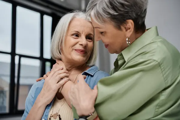 Due donne mature si abbracciano in uno studio fotografico, una tenendo l'altro collo con uno sguardo amorevole. — Foto stock