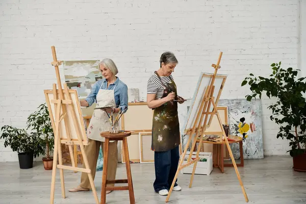 Two mature women paint at easels in an art studio. — Stock Photo