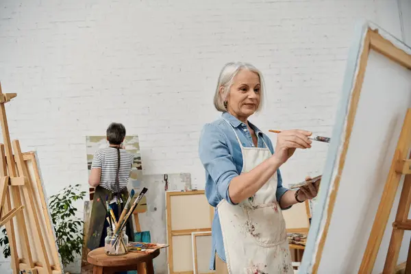 A mature lesbian couple enjoys a day of creative expression, painting together in their art studio. — Stock Photo