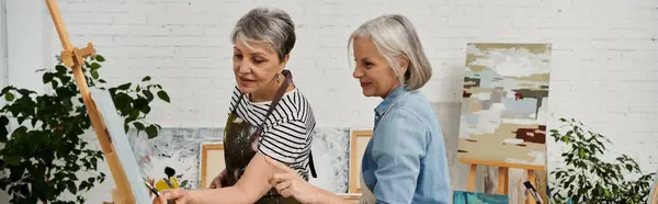 Two mature lesbian women paint together in a light-filled art studio, sharing artistic passion and skill. — Stock Photo