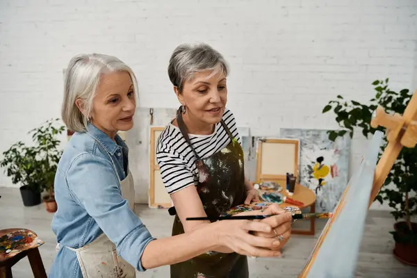 A lesbian couple paints together in a bright art studio, sharing a moment of creativity and connection. — Stock Photo