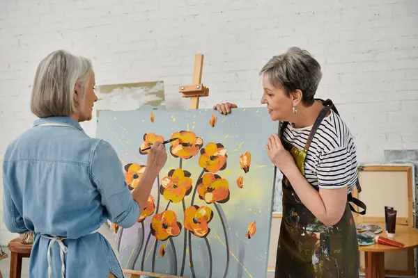 Two mature women in an art studio, painting together and sharing a lighthearted moment. — Stock Photo