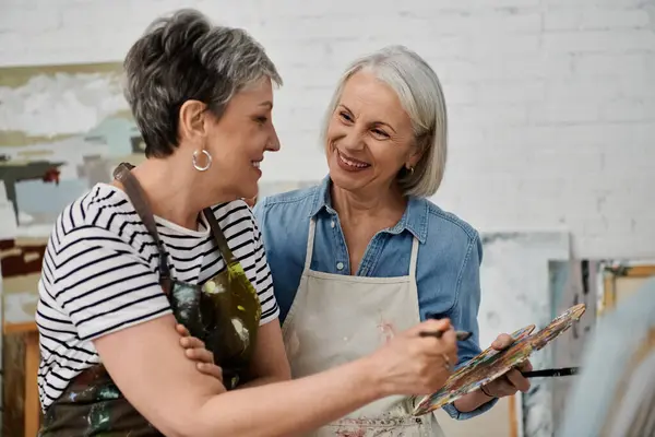 A mature lesbian couple in an art studio, painting together and sharing a happy moment. — Stock Photo