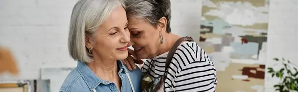 A mature lesbian couple stands together in their art studio, embracing the joys of creating and learning new skills. — Stock Photo