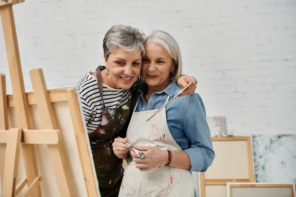 A lesbian couple paints side by side in an art studio, sharing a smile and a moment of creative connection. — Stock Photo