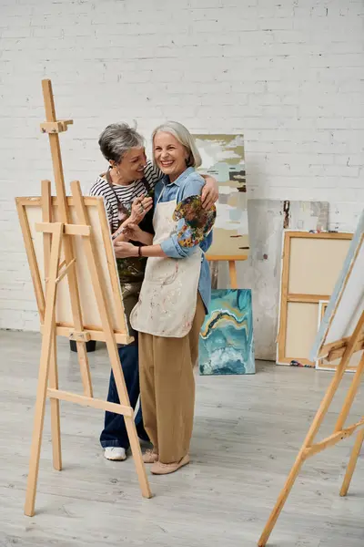 Due donne stanno insieme in uno studio d'arte, una sorridente e con una tavolozza in mano. — Foto stock