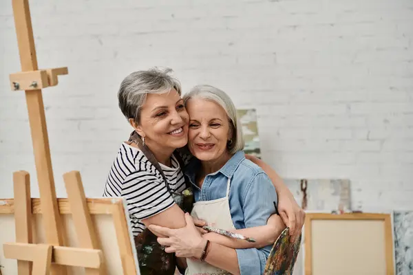 Two women, embraced in an art studio, share a moment of love and joy as they paint and learn together. — Stock Photo