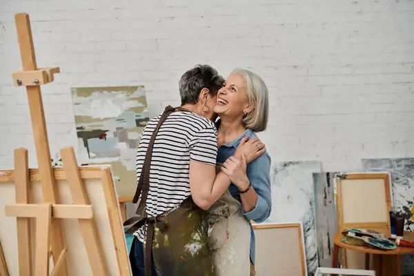 A loving lesbian couple embrace in an art studio, their shared passion for painting bringing them closer. — Stock Photo