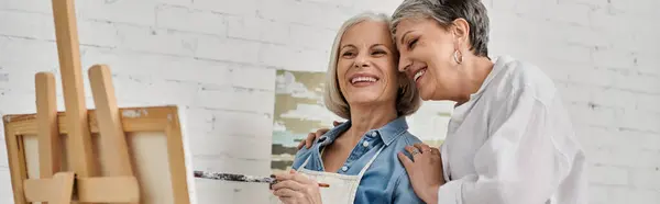 Two women in a studio, one painting, the other smiling and offering support. — Stock Photo
