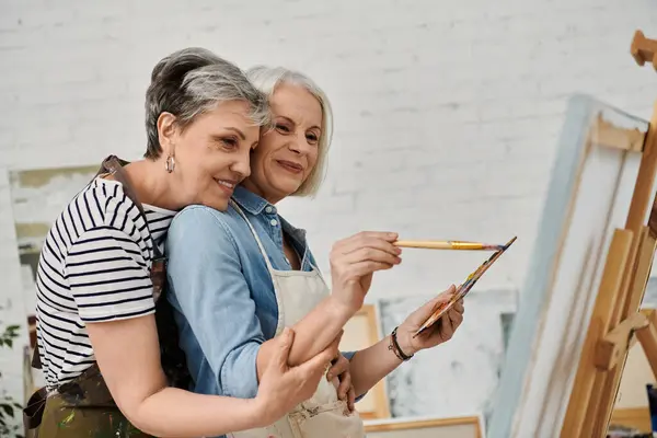 A lesbian couple embraces in a studio, one woman painting while the other watches with a smile. — Stock Photo