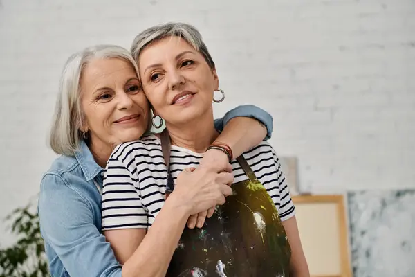 Two mature women, a lesbian couple, embrace in their art studio. — Stock Photo