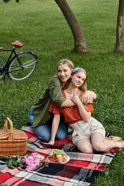 Two young women are enjoying a picnic in a green park, embracing and sharing a smile. — Stock Photo