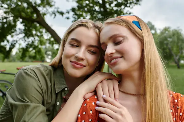 Two young women, dressed casually, share a tender moment in a green park. — Stock Photo