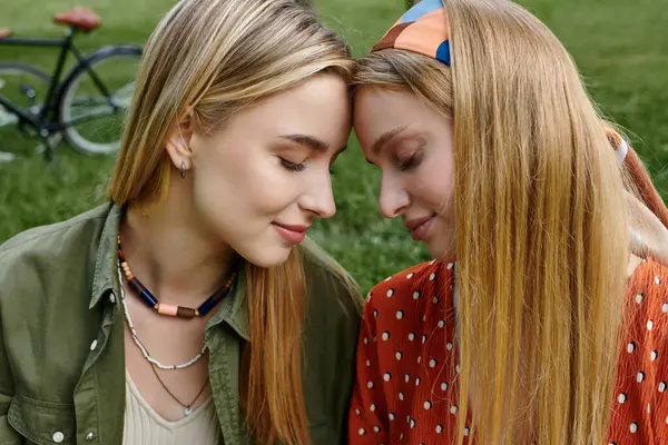 A young lesbian couple shares a tender moment in a green park, their foreheads touching, eyes closed. — Stock Photo