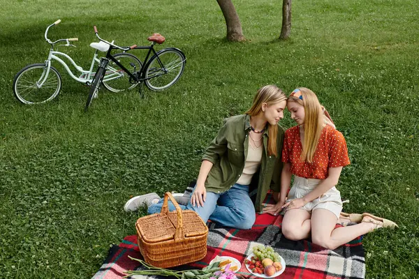 A lesbian couple shares a tender moment during a picnic in a lush green park. — Stock Photo