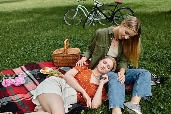 Two women share a romantic moment on a picnic blanket in a green park. — Stock Photo