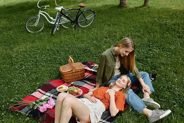 Dos mujeres disfrutan de un picnic en un parque, una tumbada mientras la otra la mira cariñosamente. - foto de stock