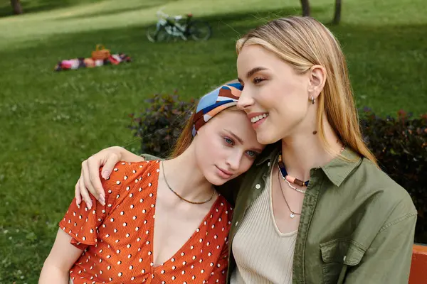 A youthful lesbian couple cuddles in a lush park, one woman in a red polka-dot dress resting her head on her partners shoulder — Stock Photo