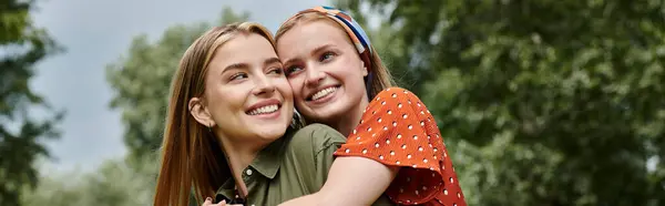 Two young women smile and hug in a green park on a sunny day. — Stock Photo