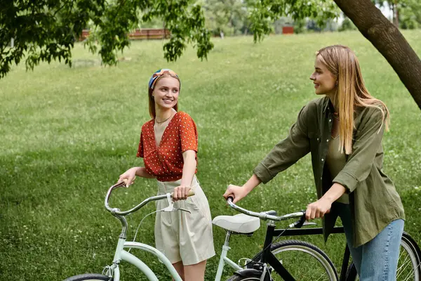 Zwei Frauen auf einer romantischen Radtour, die einander in einem Rasenpark anlächeln. — Stock Photo